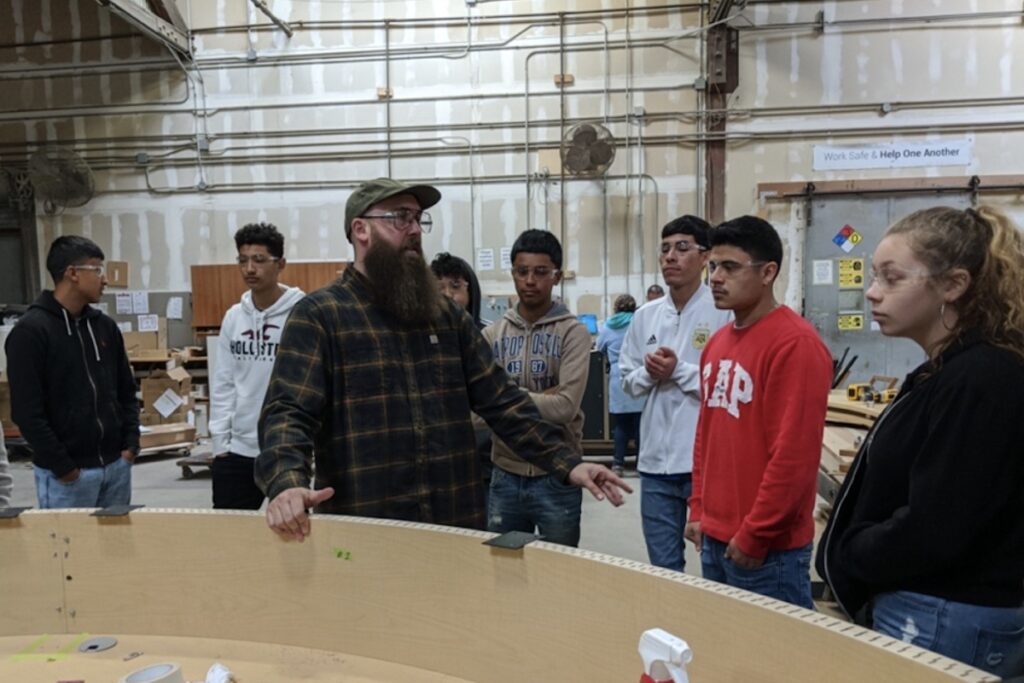 High school students listen as a worker at Creative Wood explains how to make a rounded reception desk during a Manufacturing Day factory tour in 2019.